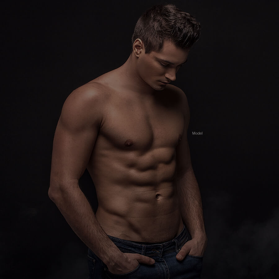 male model looking down shirtless with hands in pockets