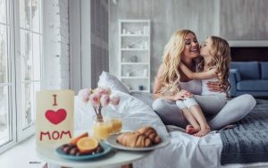 Attractive young blonde mother embraces her young daughter with a mother's day card in the foreground of the picture.